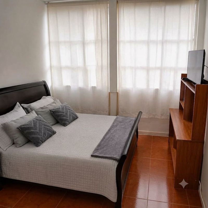Urban: cama con cortinas largas y televisor sobre consola de madera.